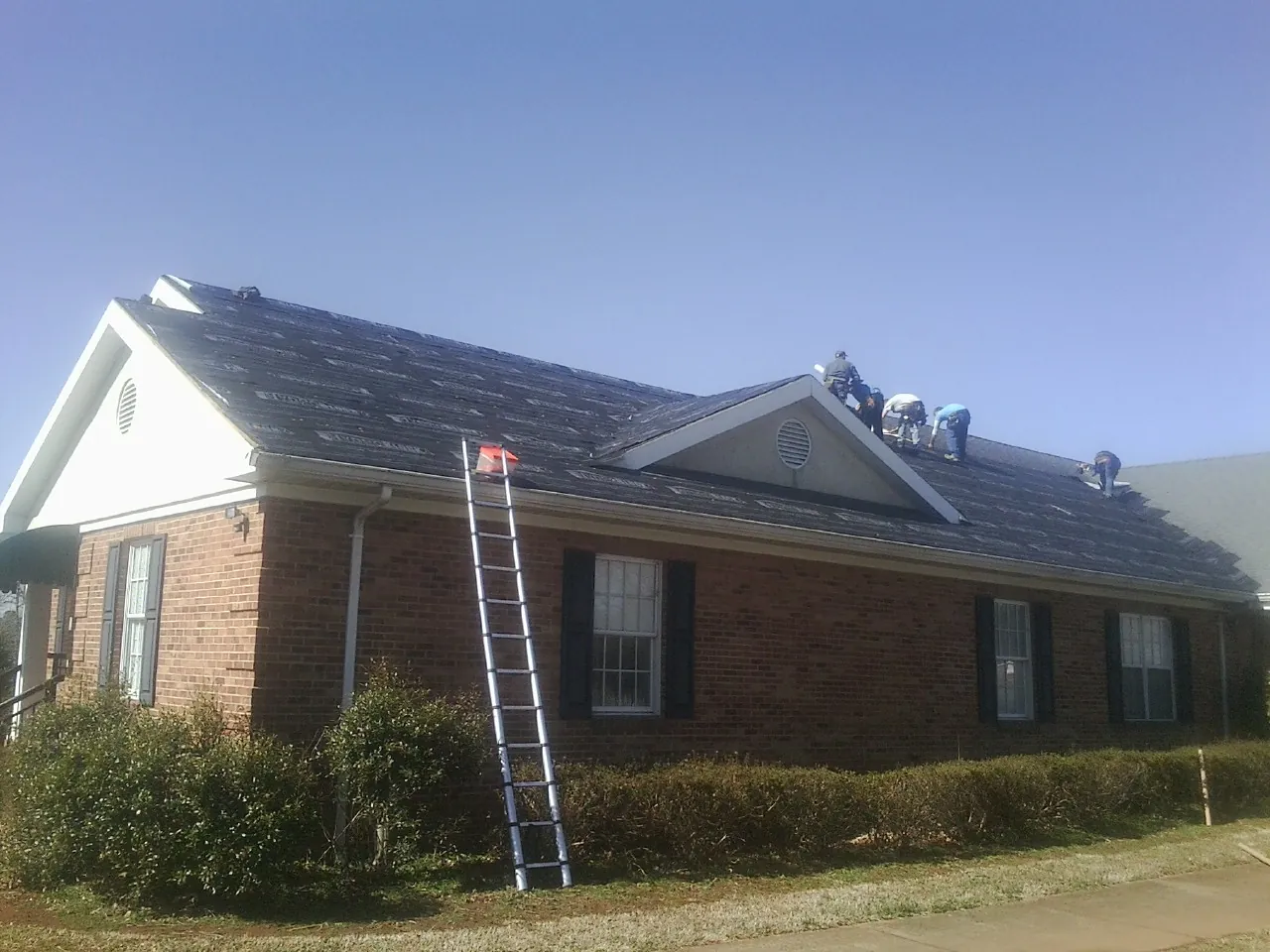 Crew tearing shingles off a brick ranch roof with a ladder set — Metal Roof Repair work by our crew in Clarkia