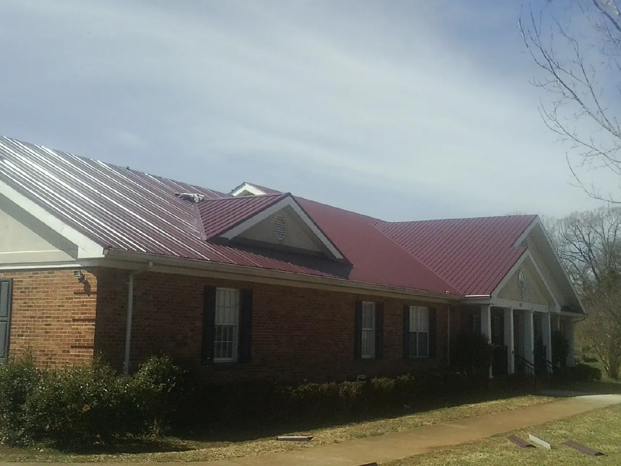 Red metal roof with gabled entries on a long brick building, from a Hail Damage Roof Repair job in Clarkia