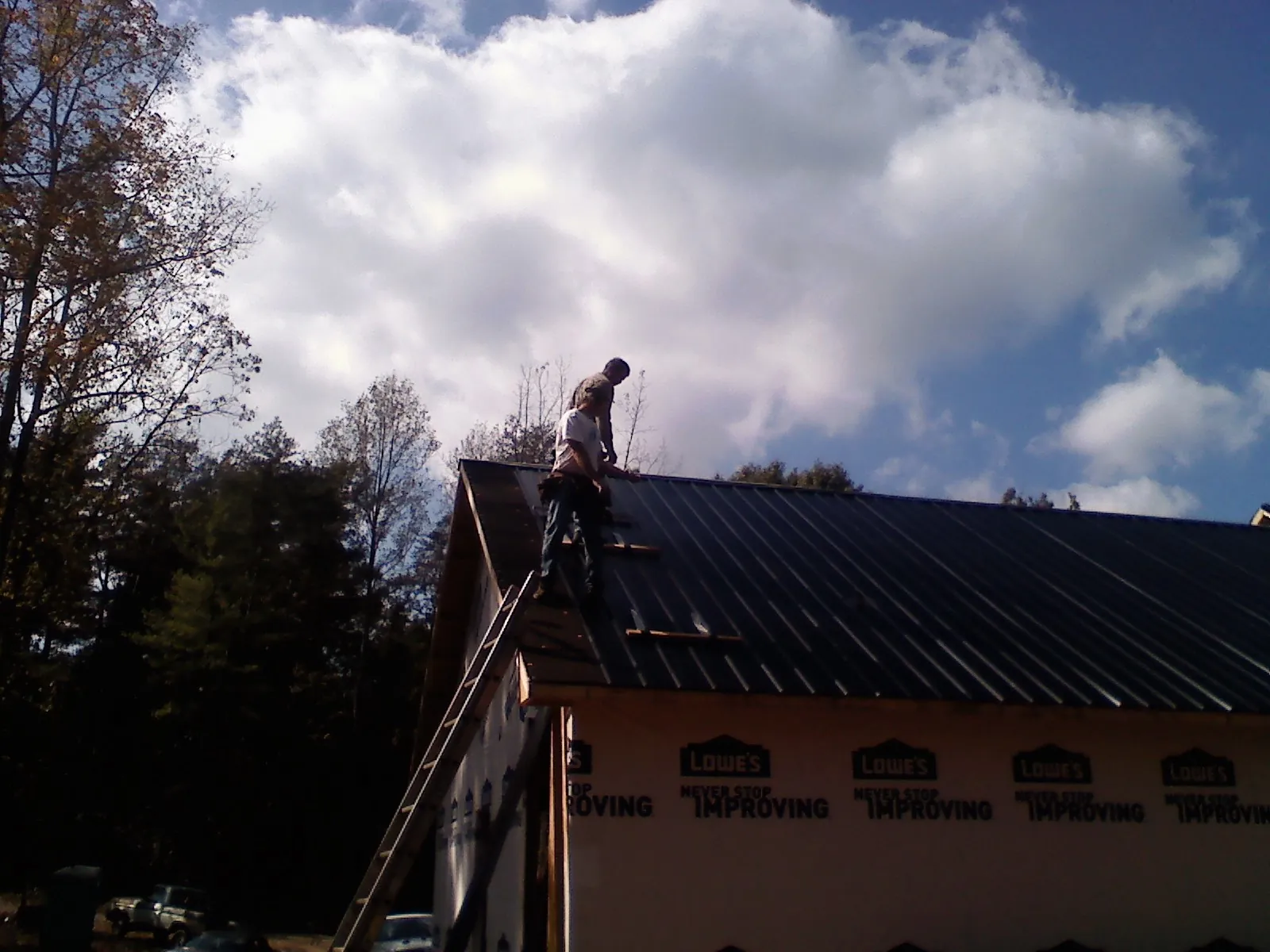 Roofer fastening dark metal panels high against a cloudy sky, from a Roof Inspection job in Clarkia