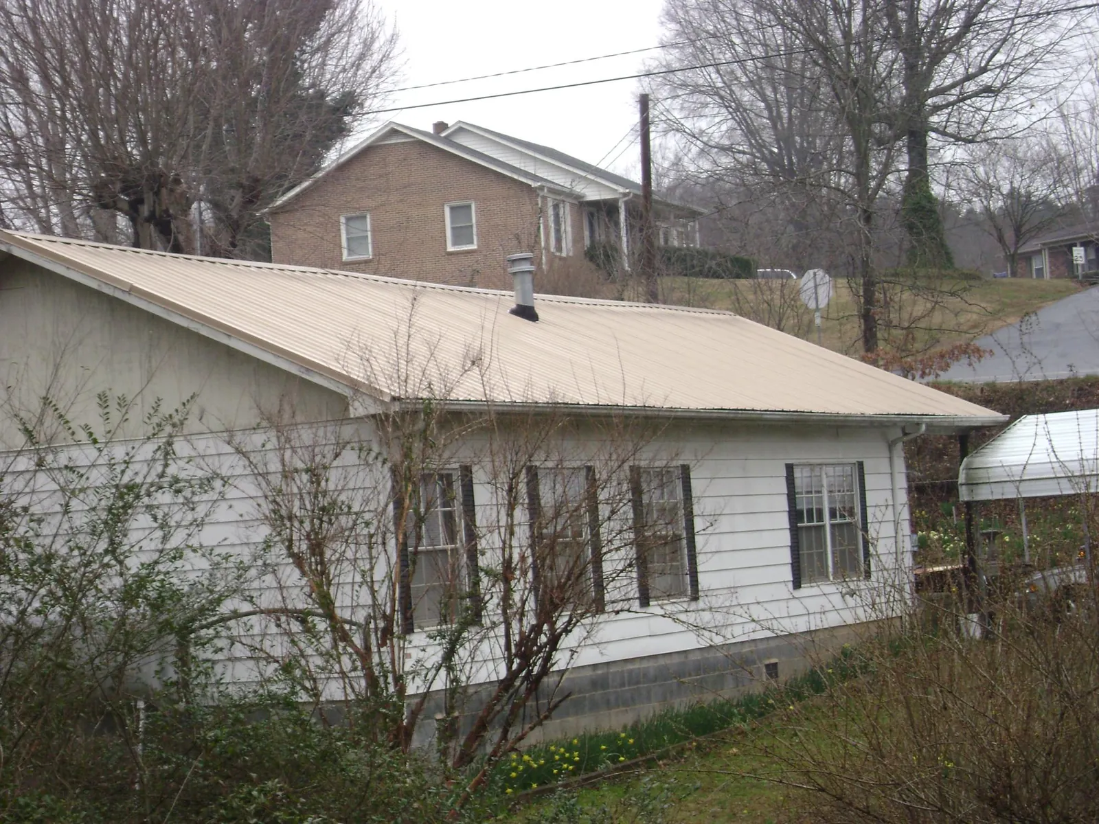 Tan metal roof on a white sided house set into a hillside — Commercial Roofing by Roofing Brothers in Clarkia